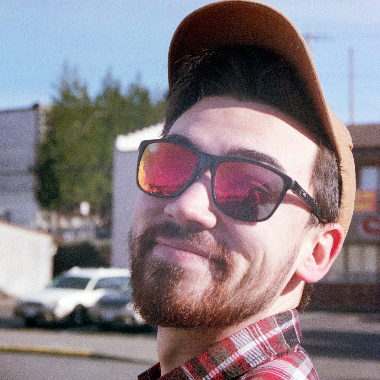 A picture of me wearing red sunglasses and a hat, smiling at the camera.